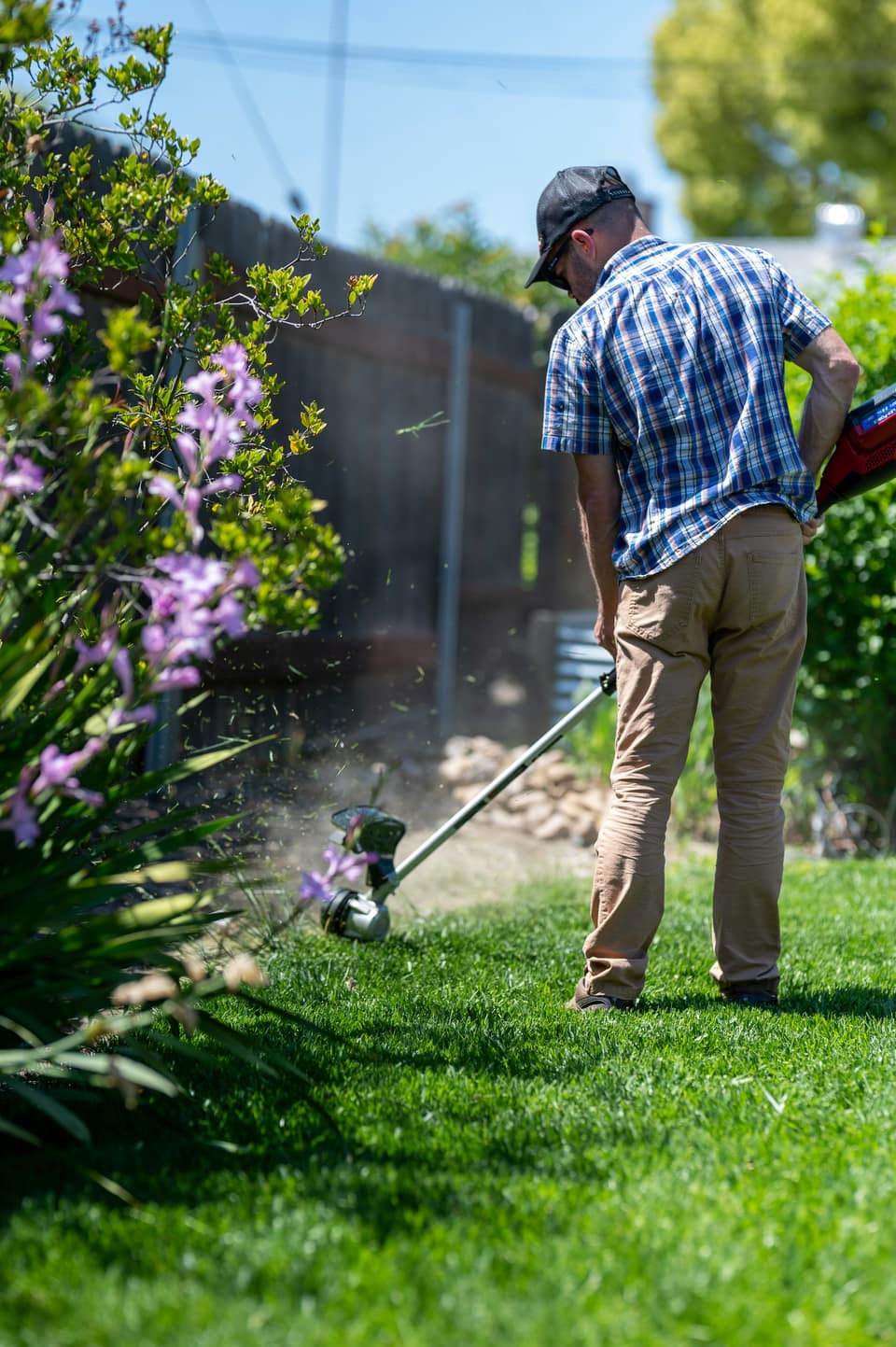 A landscaper using a string trimmer to edge a lawn beside a flower bed.