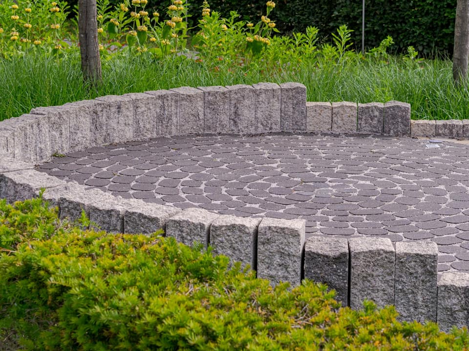 A circular paver patio ringed by a low stone wall and green shrubs.